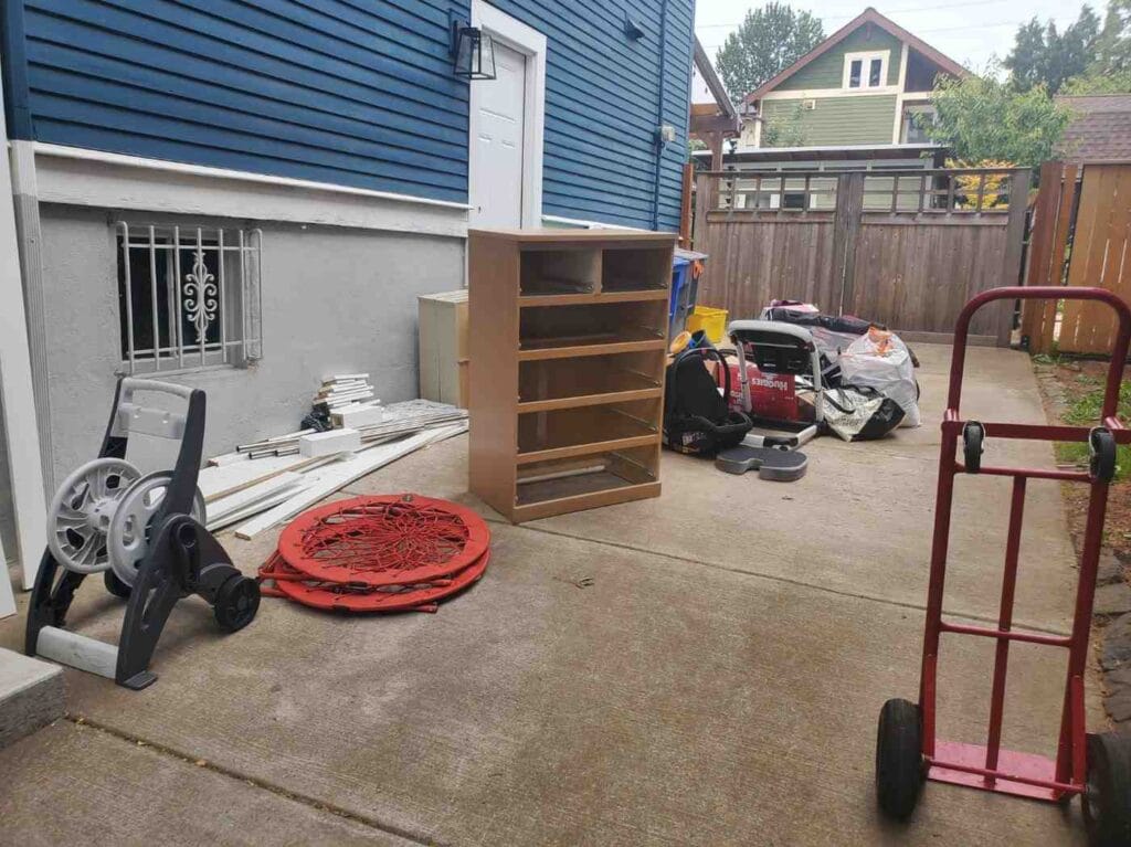 Driveway clutter including an old dresser, discarded household items, and a red hand truck before professional junk removal service.